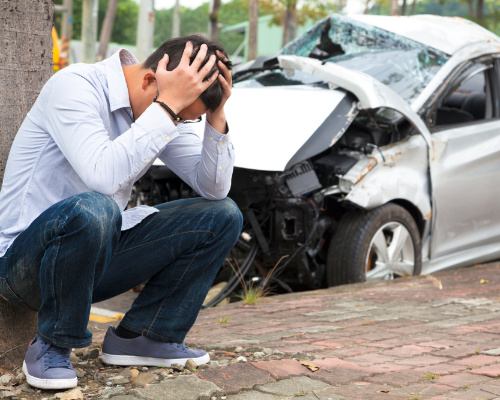 man next to totaled car after getting into an accident from driving recklessly