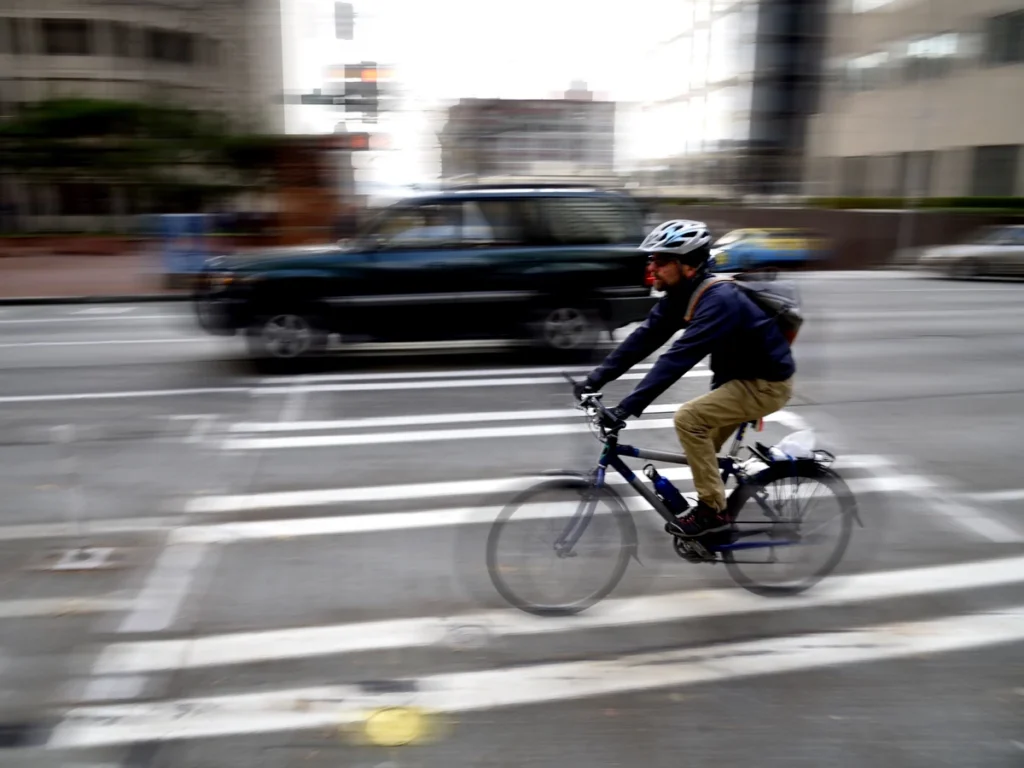 Cyclist riding through a crosswalk as an SUV passes on a city street