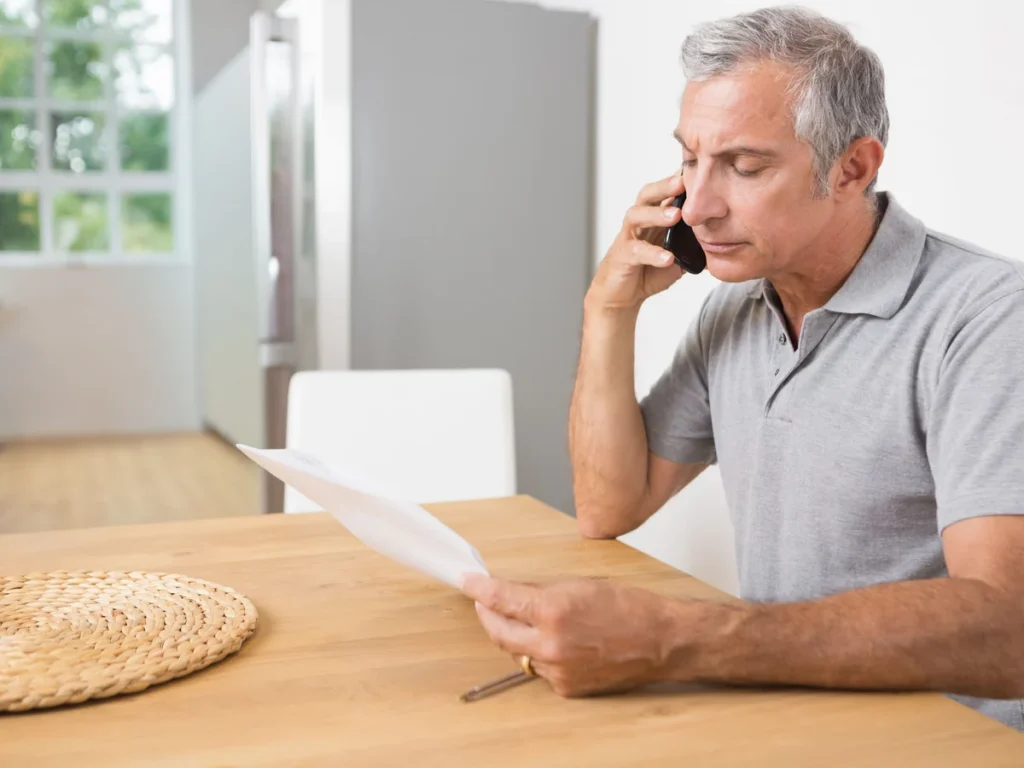 Man on the phone with an insurance adjuster while reading a letter at his kitchen table