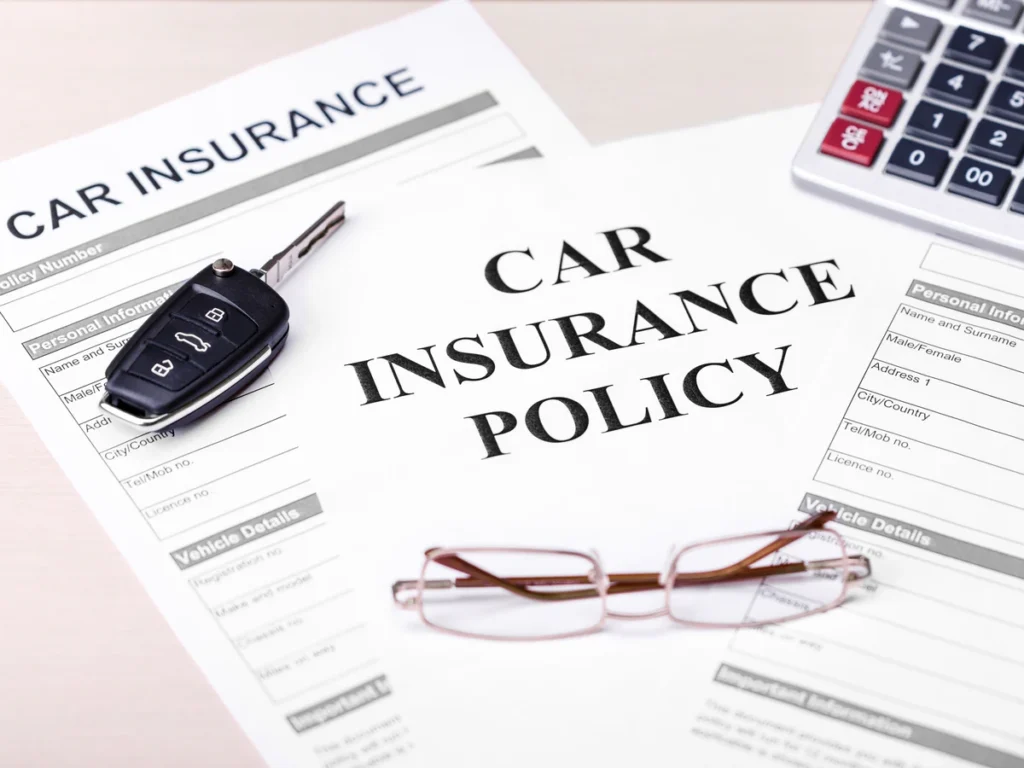 Car insurance policy papers with a key fob, glasses and a calculator on a desk