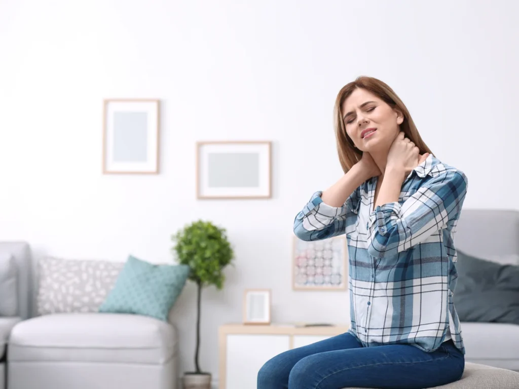 Woman holding her neck in pain while sitting in her living room